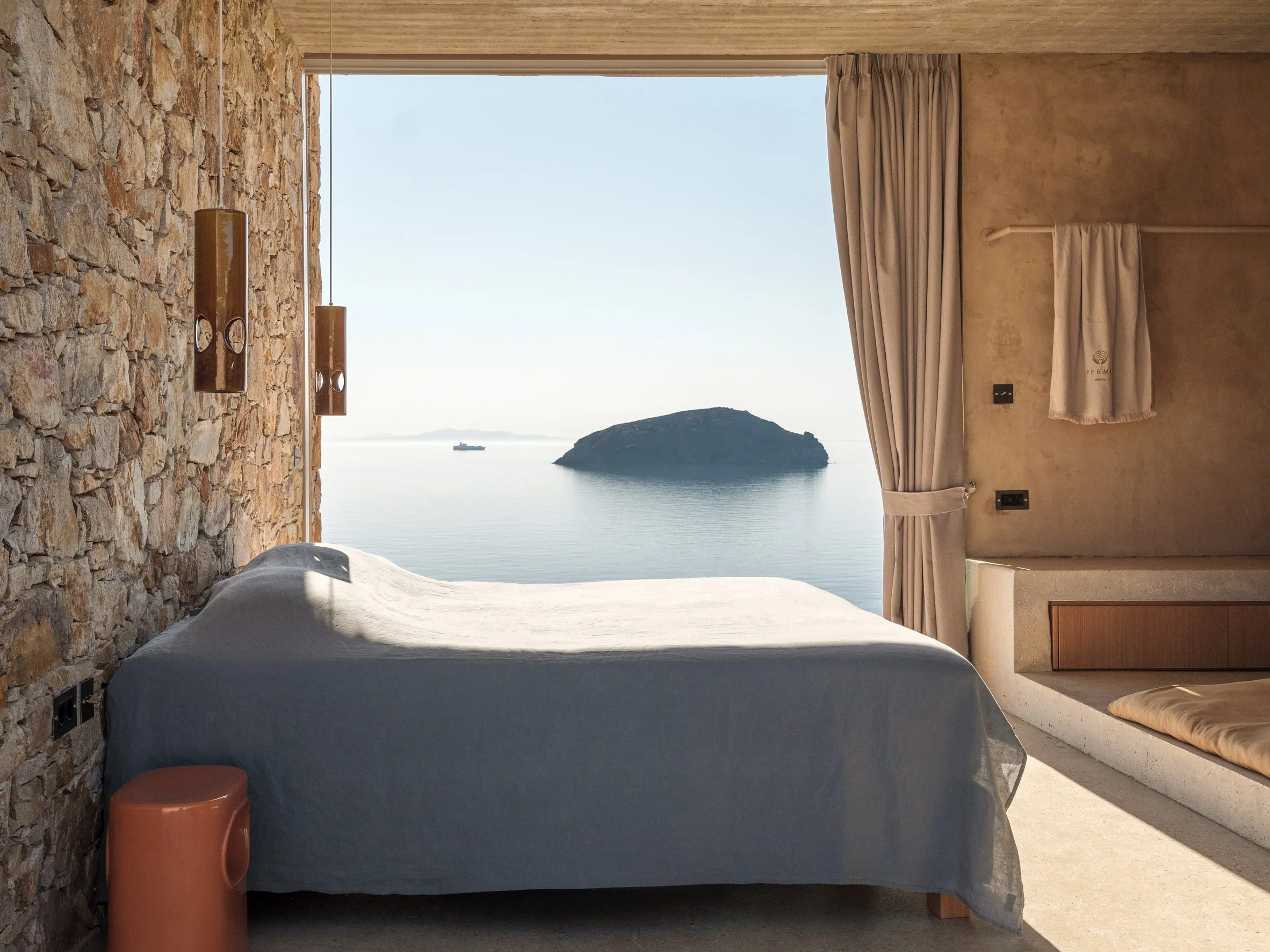 Bedroom with stone wall and large opening framing a view of the Aegean Sea