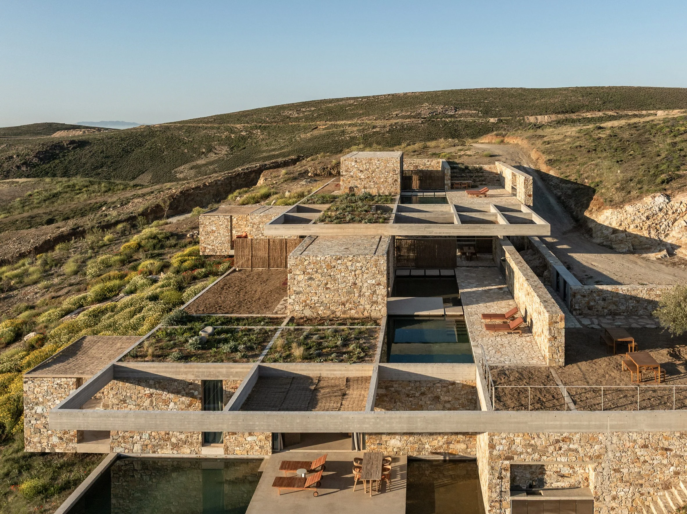 Stone-clad buildings and planted roofs arranged beneath a concrete grid structure