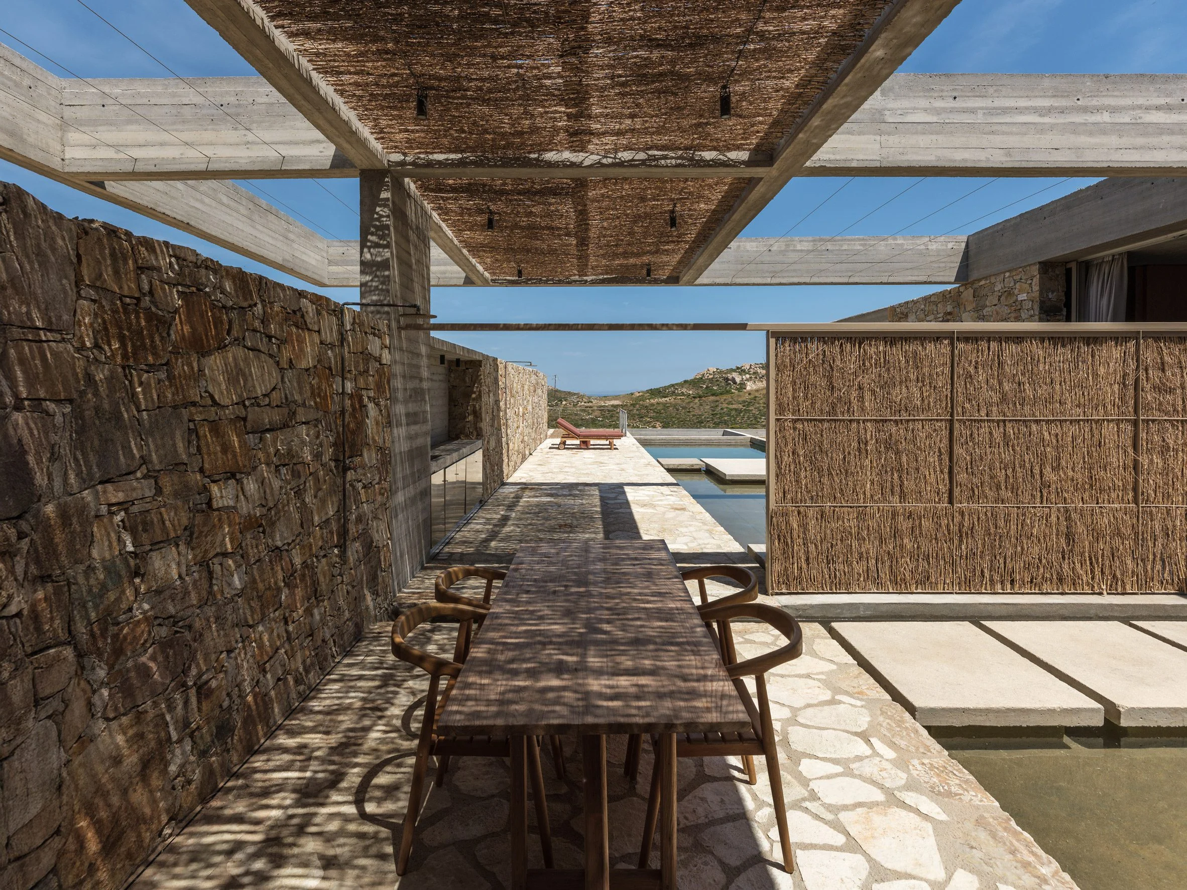 Outdoor dining space shaded by reed screens and framed by stone walls