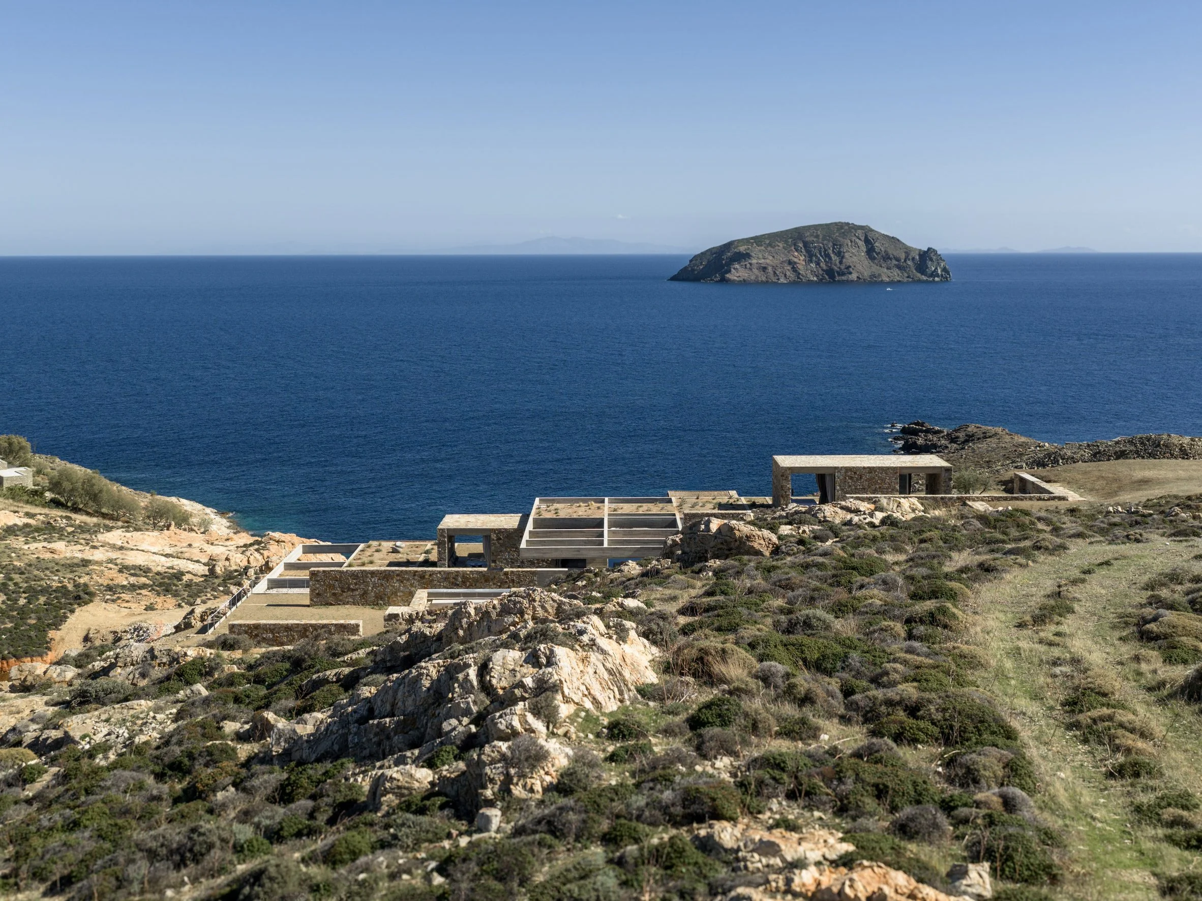 Stone accommodation units embedded into a coastal hillside overlooking the Aegean